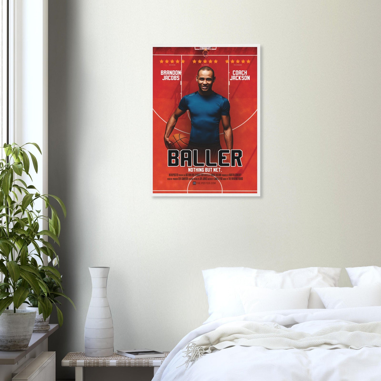 A custom basketball movie poster in a regular white frame on a grey wall above a white bed and plant