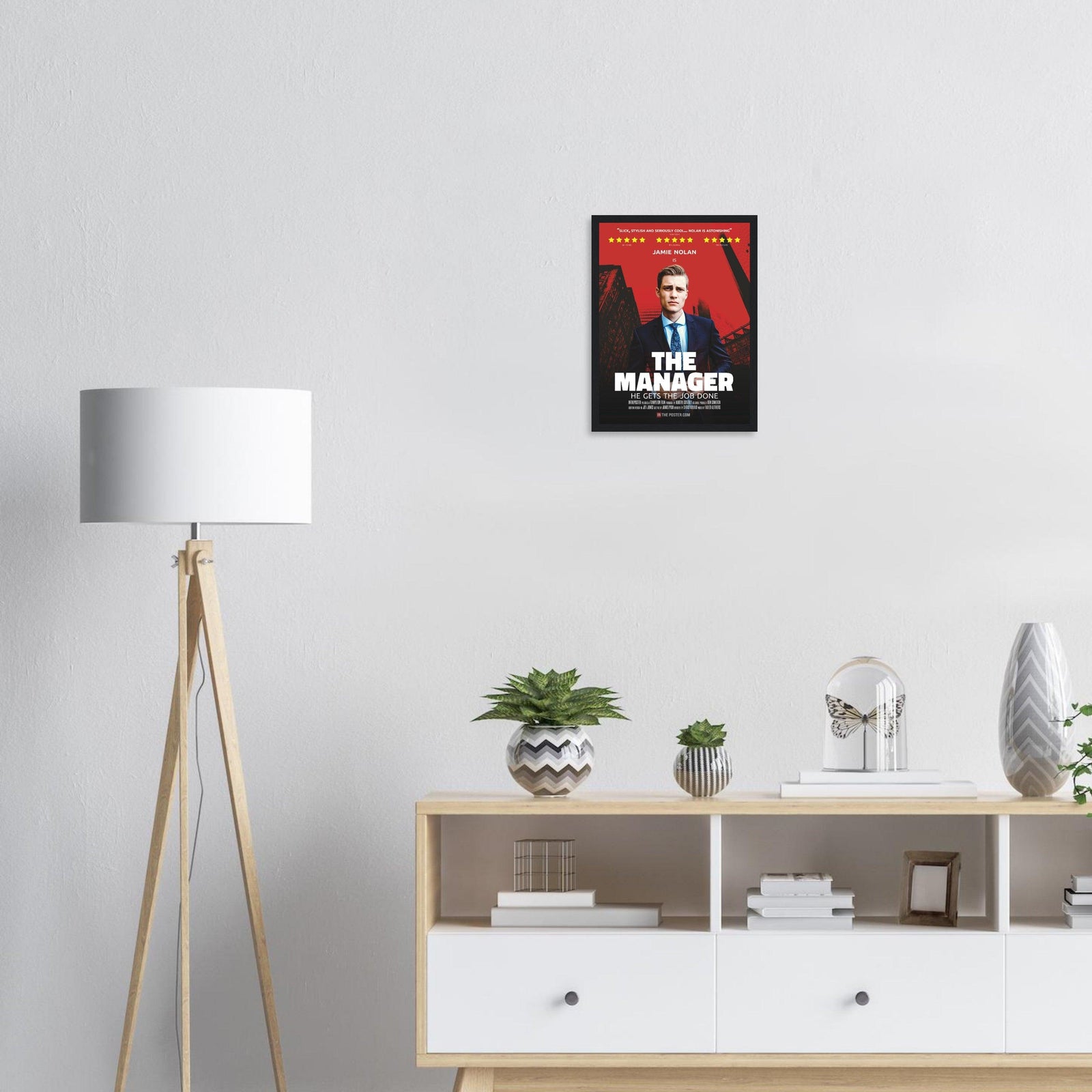 Small poster of The Manager in a black frame above a wooden cabinet and lamp