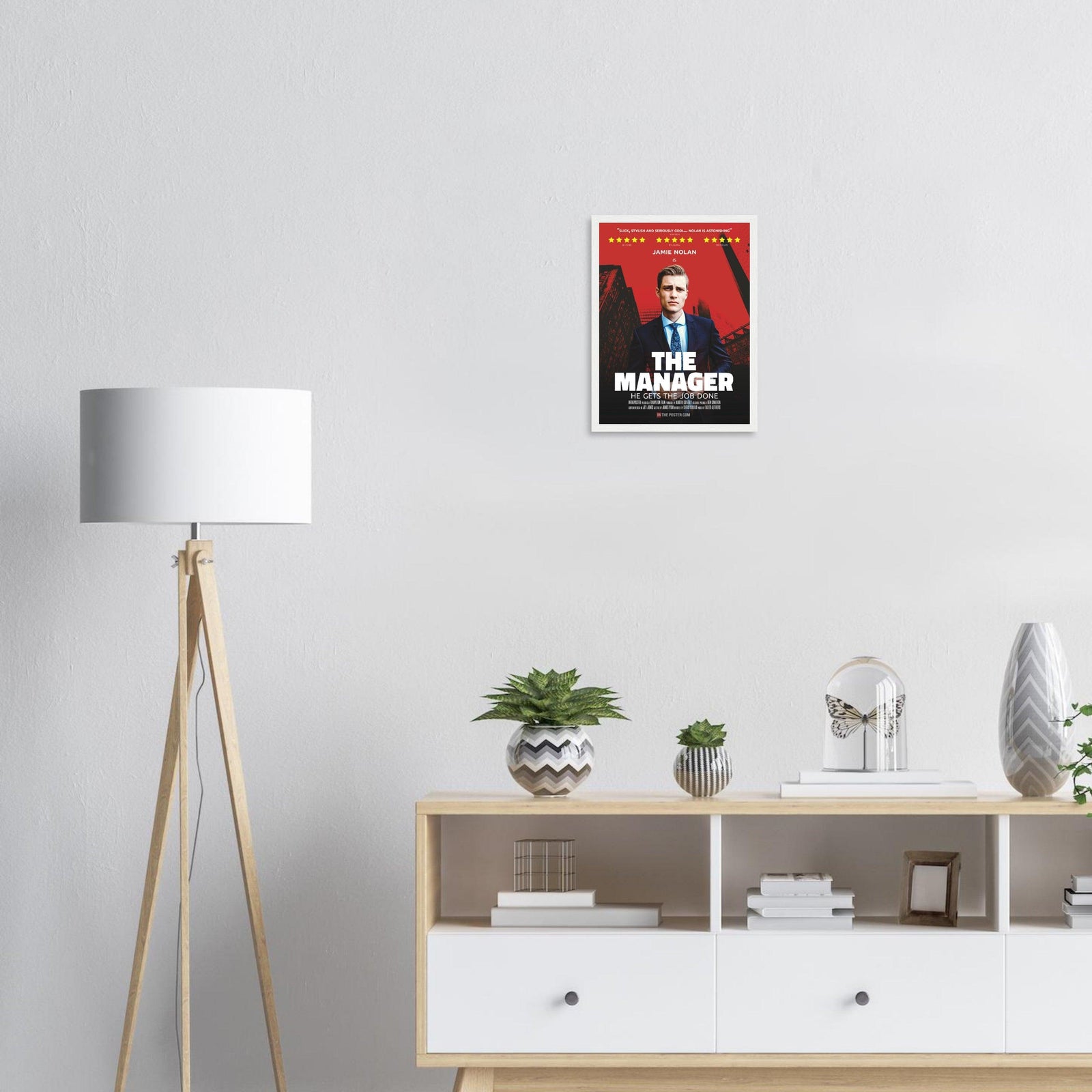 Small framed movie poster of The Manager in a white frame, above a wooden cabinet and lamp