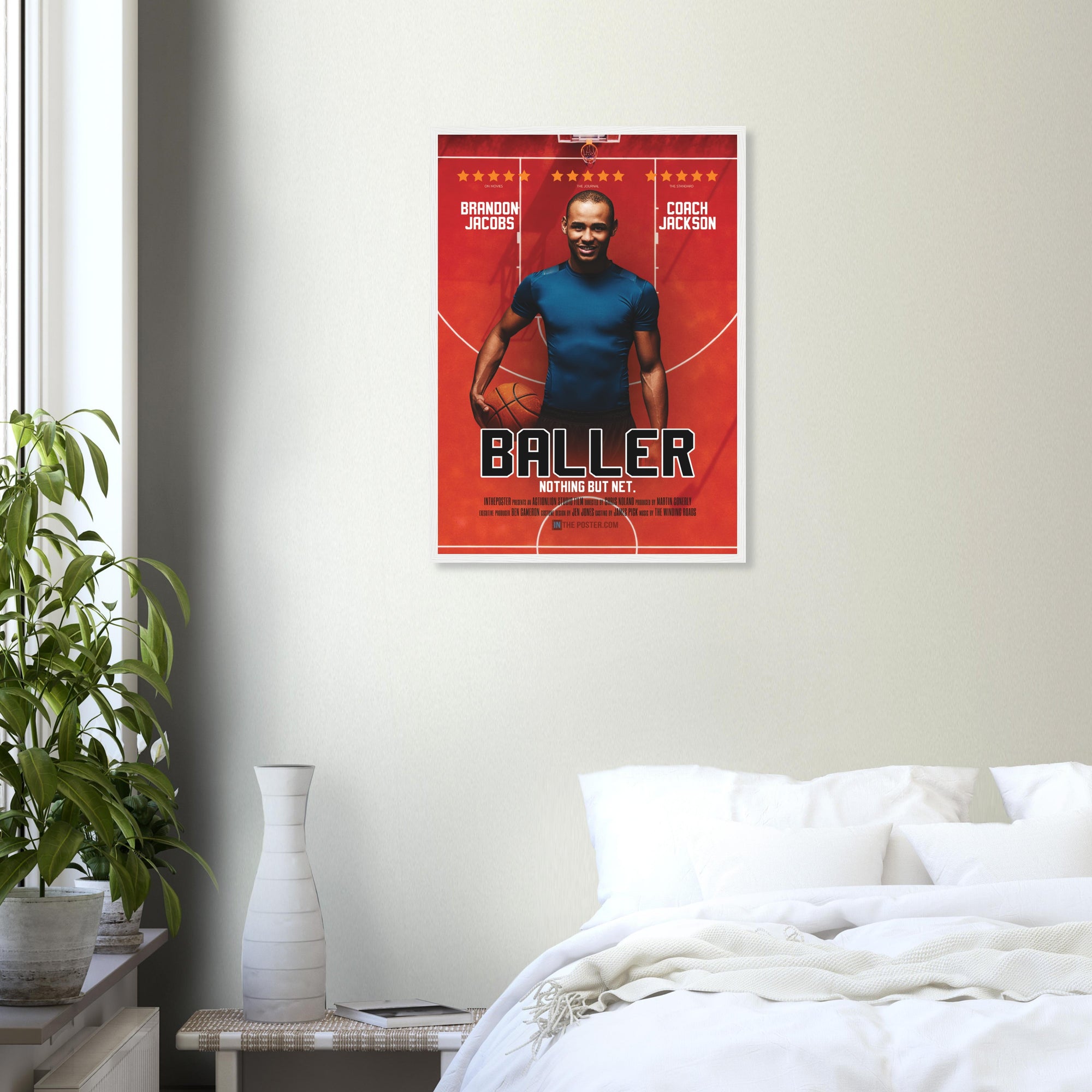 A custom basketball movie poster in a regular white frame on a grey wall above a white bed and plant