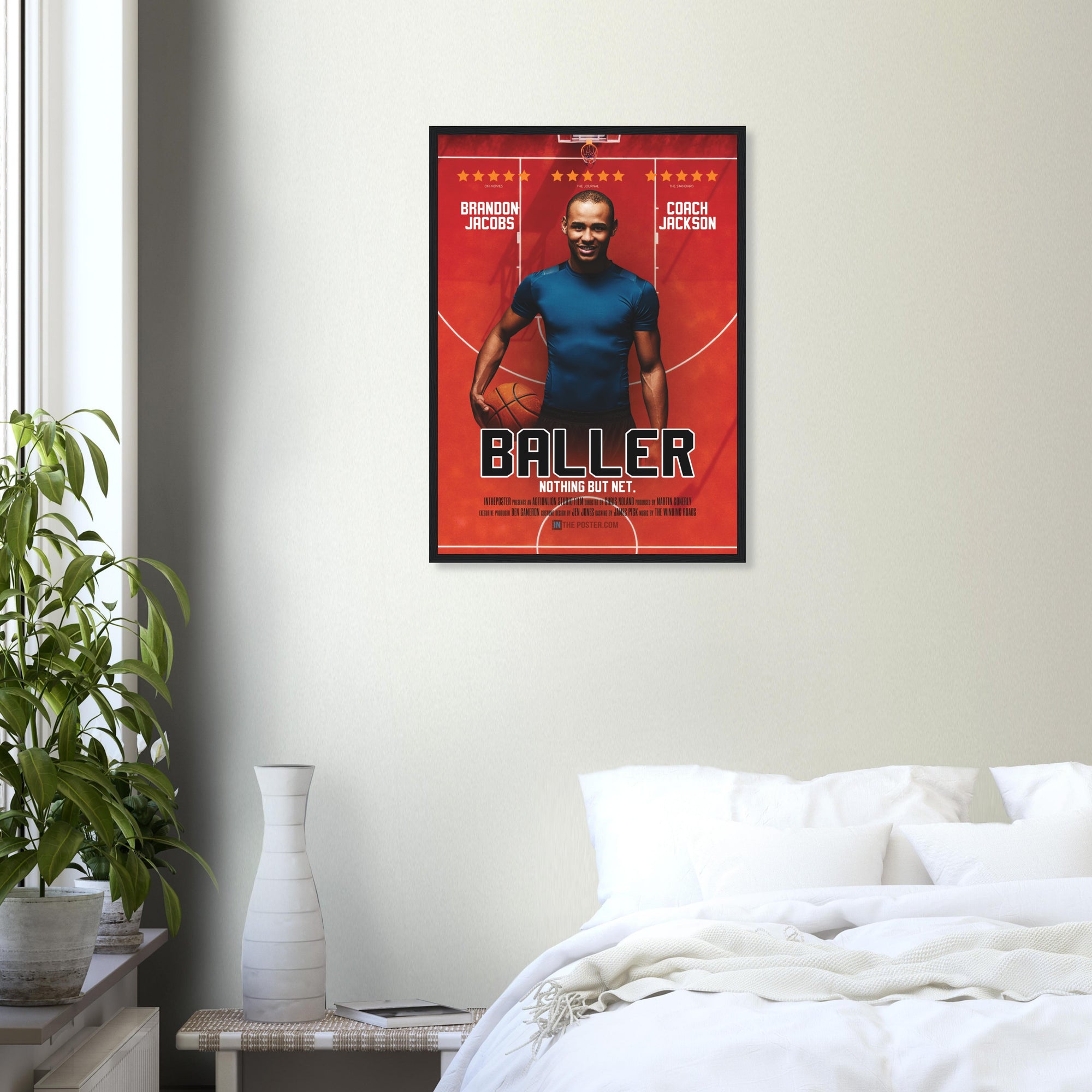 A custom basketball movie poster in a regular black frame on a grey wall above a white bed and plant