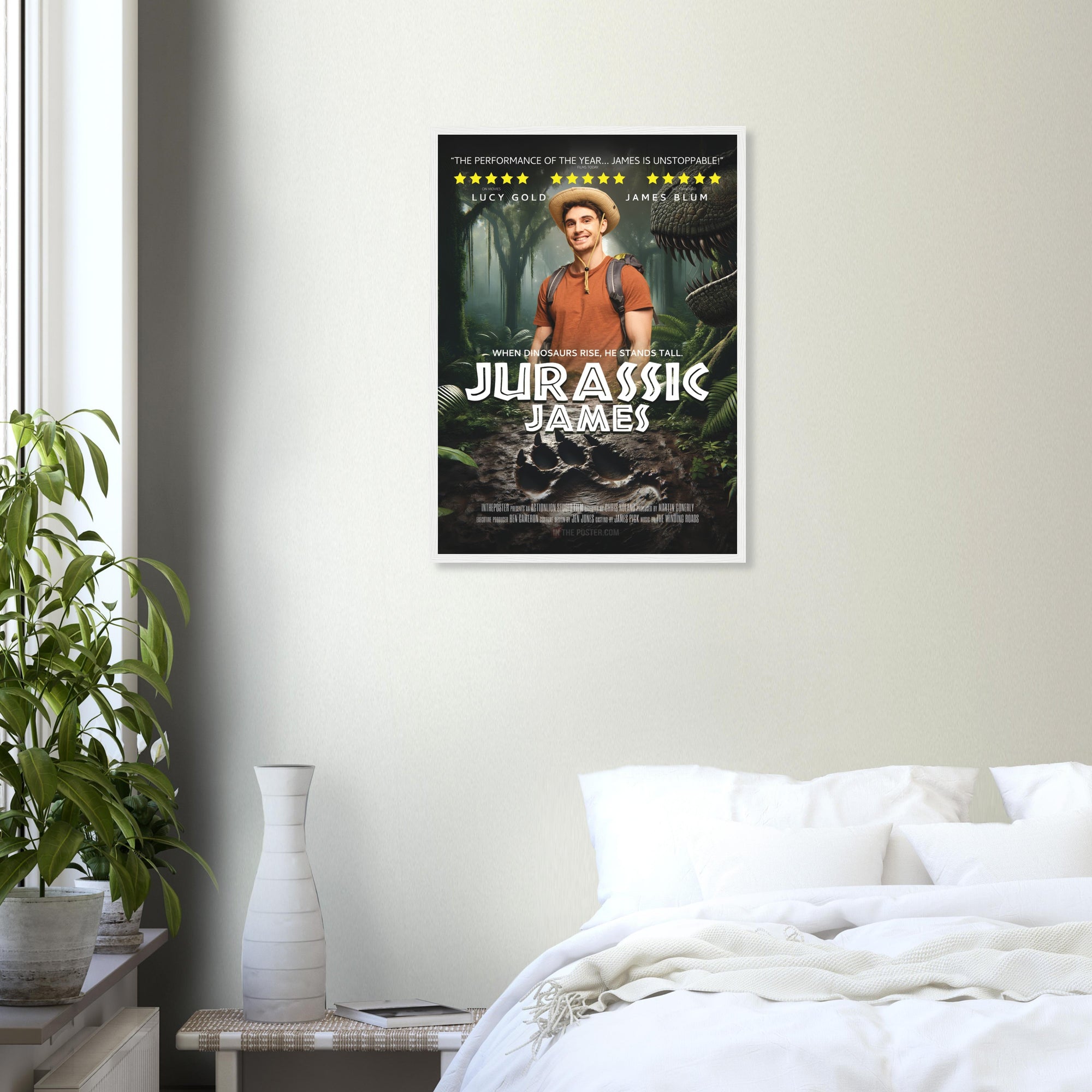 A dinosaur movie poster in a white frame is on a grey wall above a plant and a white bed.