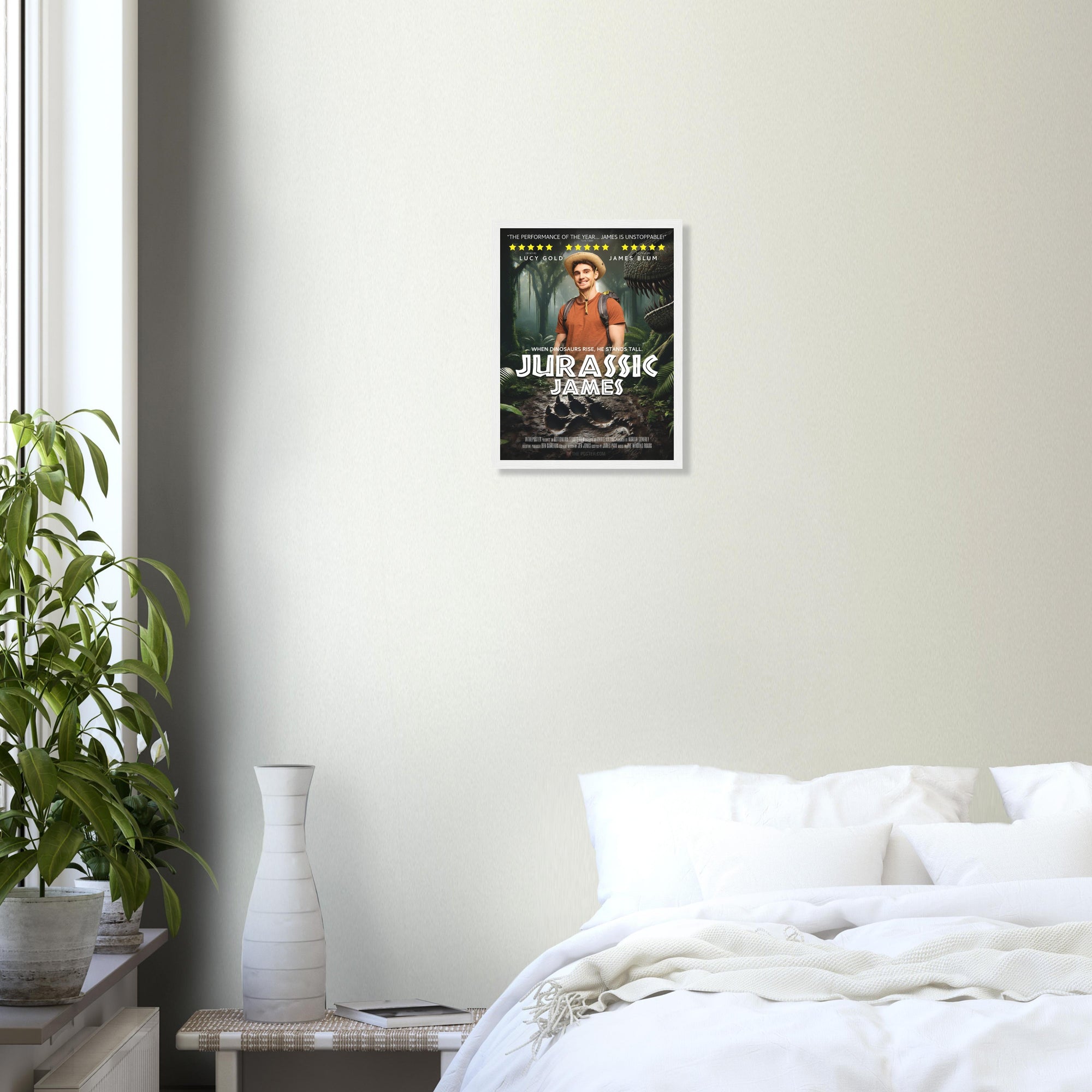 A small custom dinosaur-themed movie poster in a white frame is on a grey wall above a plant and a white bed.