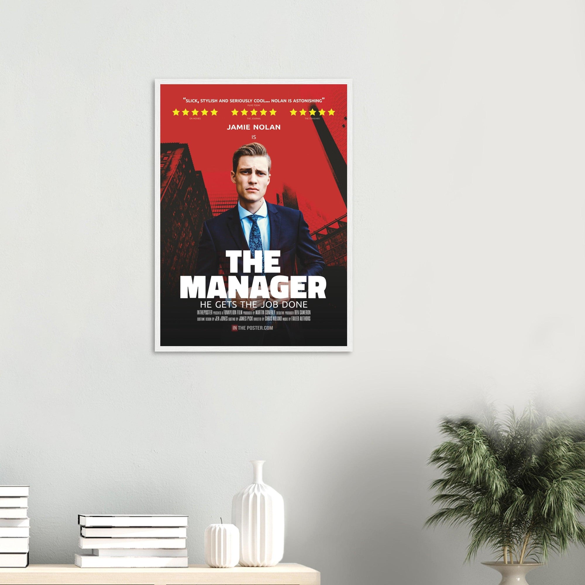 Regular framed The Manager movie poster with a white frame above a desk and a plant