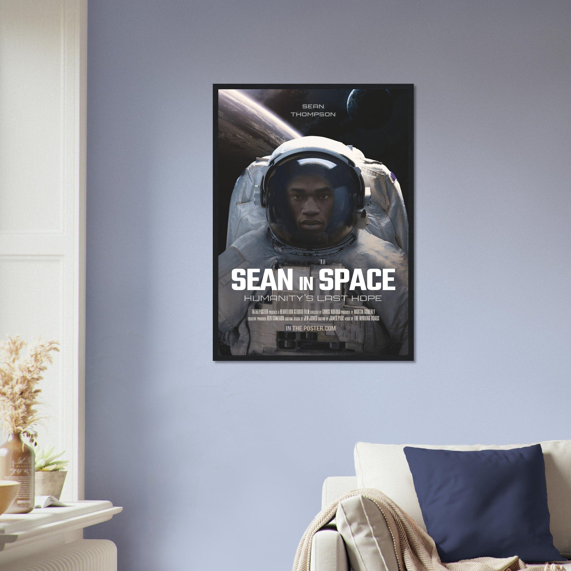 An astronaut sci-fi movie poster design in a regular black frame on a blue wall above a designer sofa