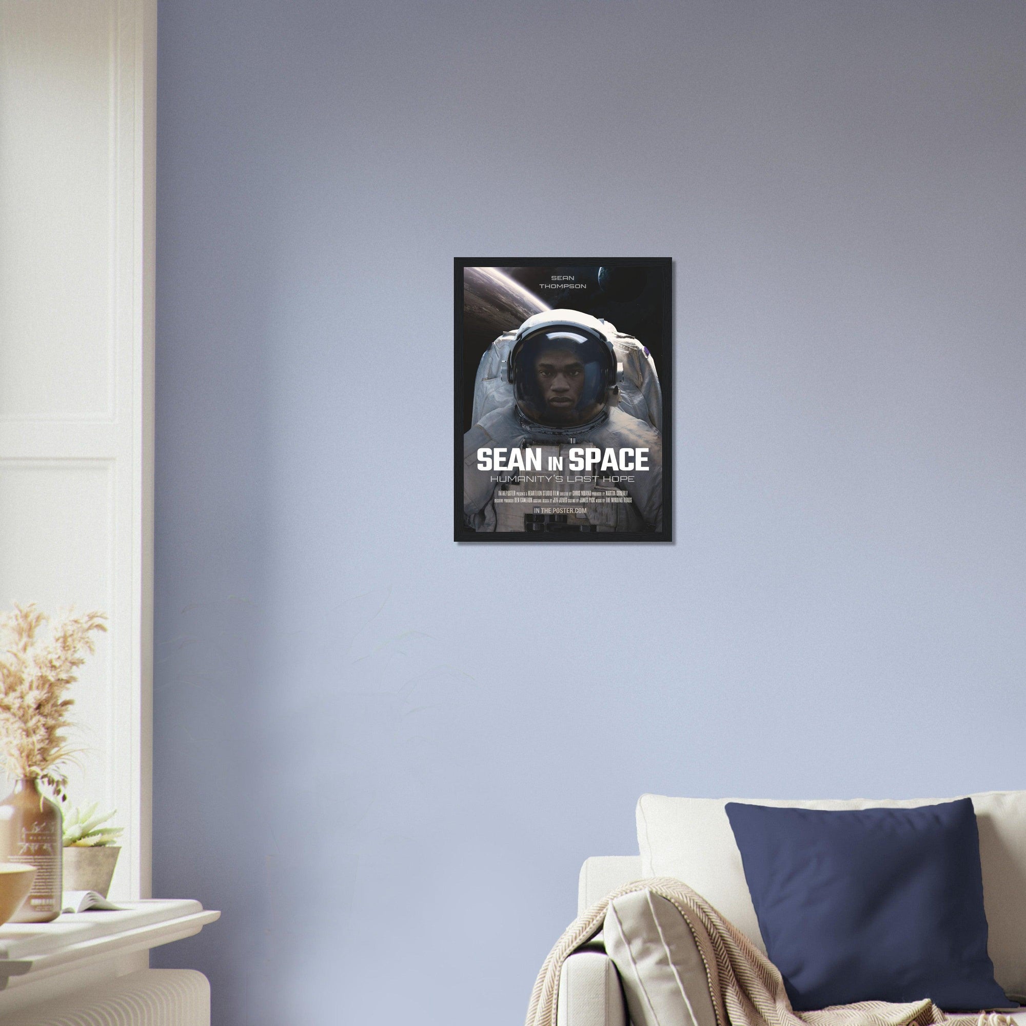 An astronaut sci-fi movie poster design in a small black frame on a blue wall above a designer sofa
