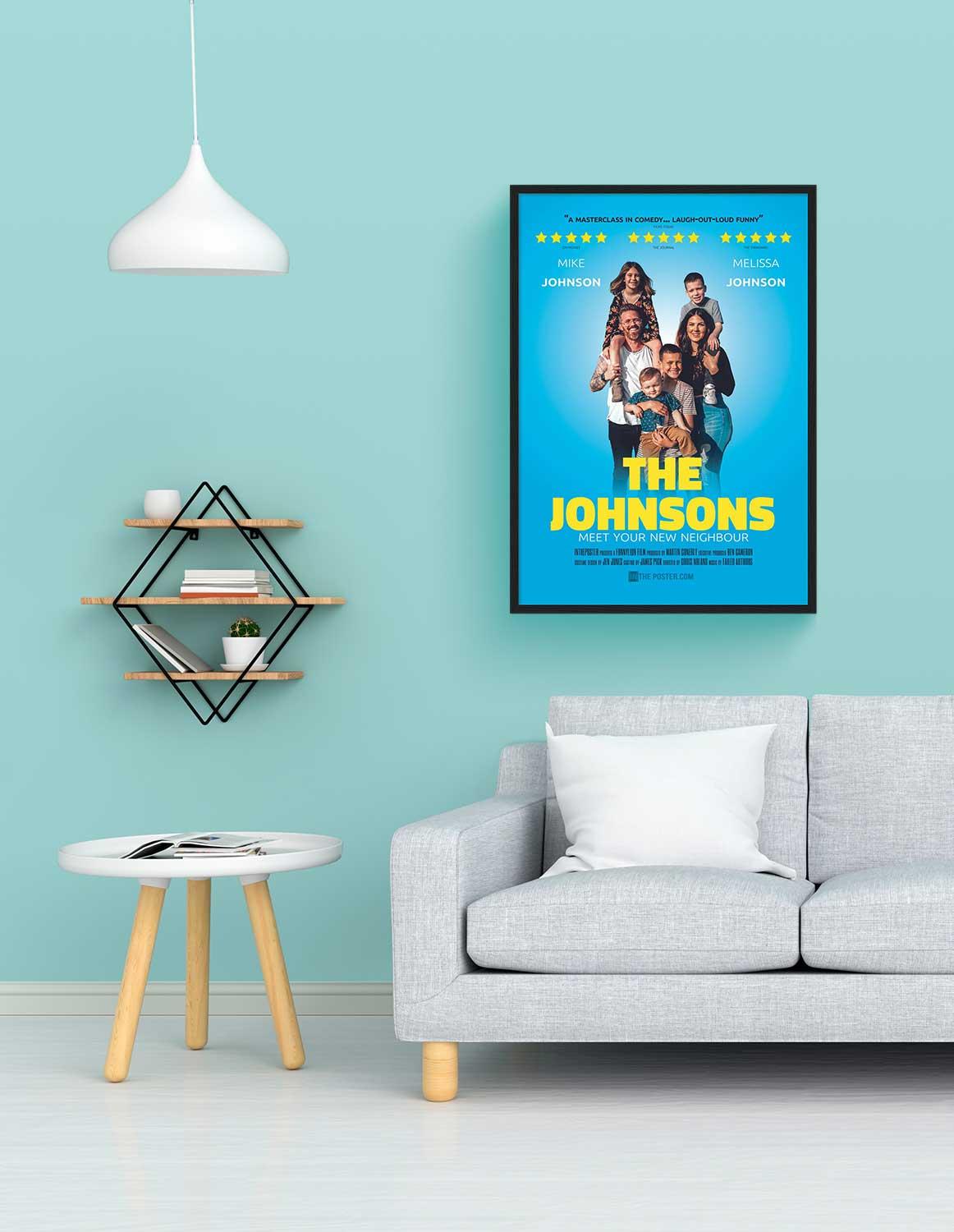 A comedy poster in a regular size black frame on the wall above a grey sofa