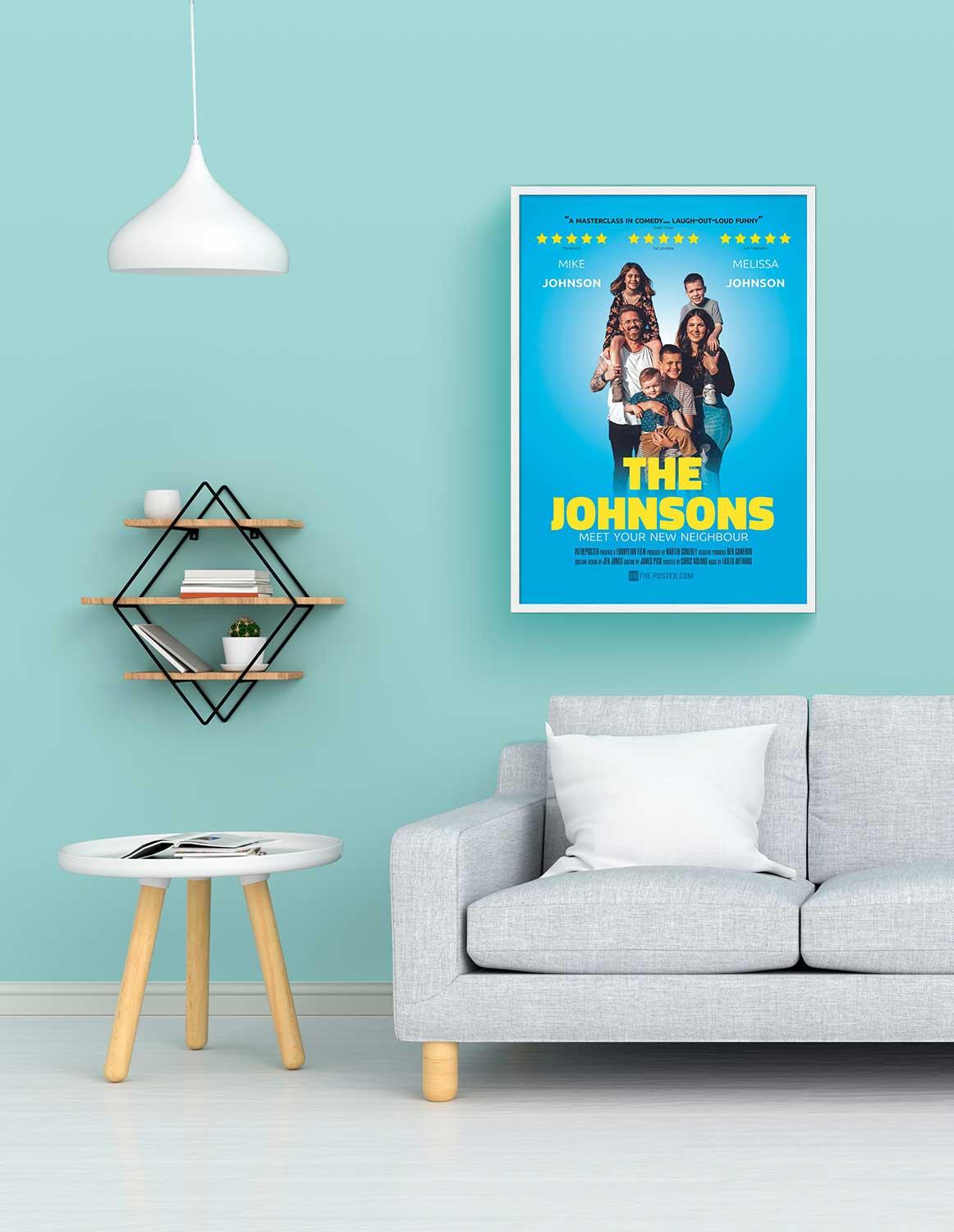 A comedy poster in a regular size white frame on the wall above a grey sofa