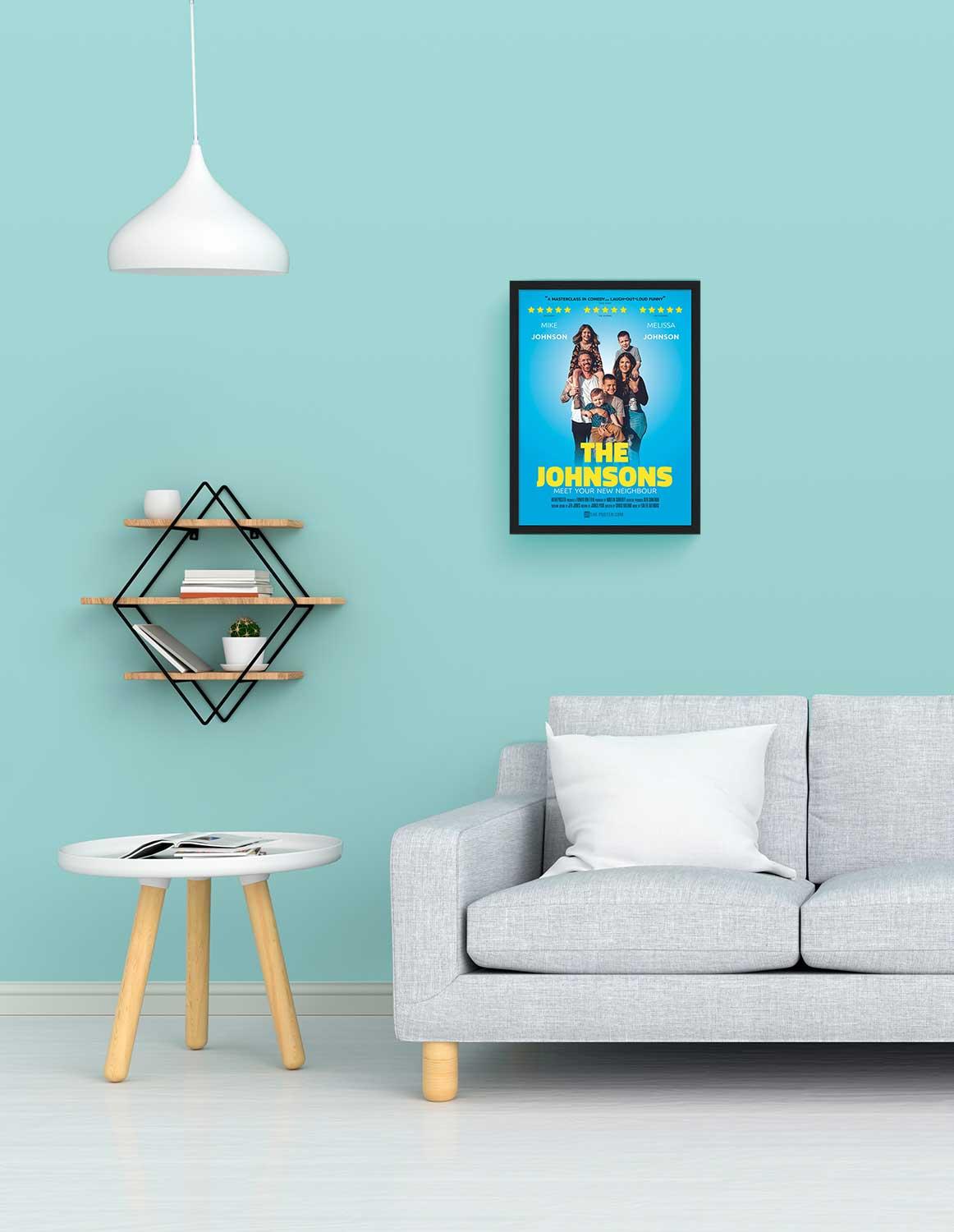 A comedy poster in a small size black frame on the wall above a grey sofa