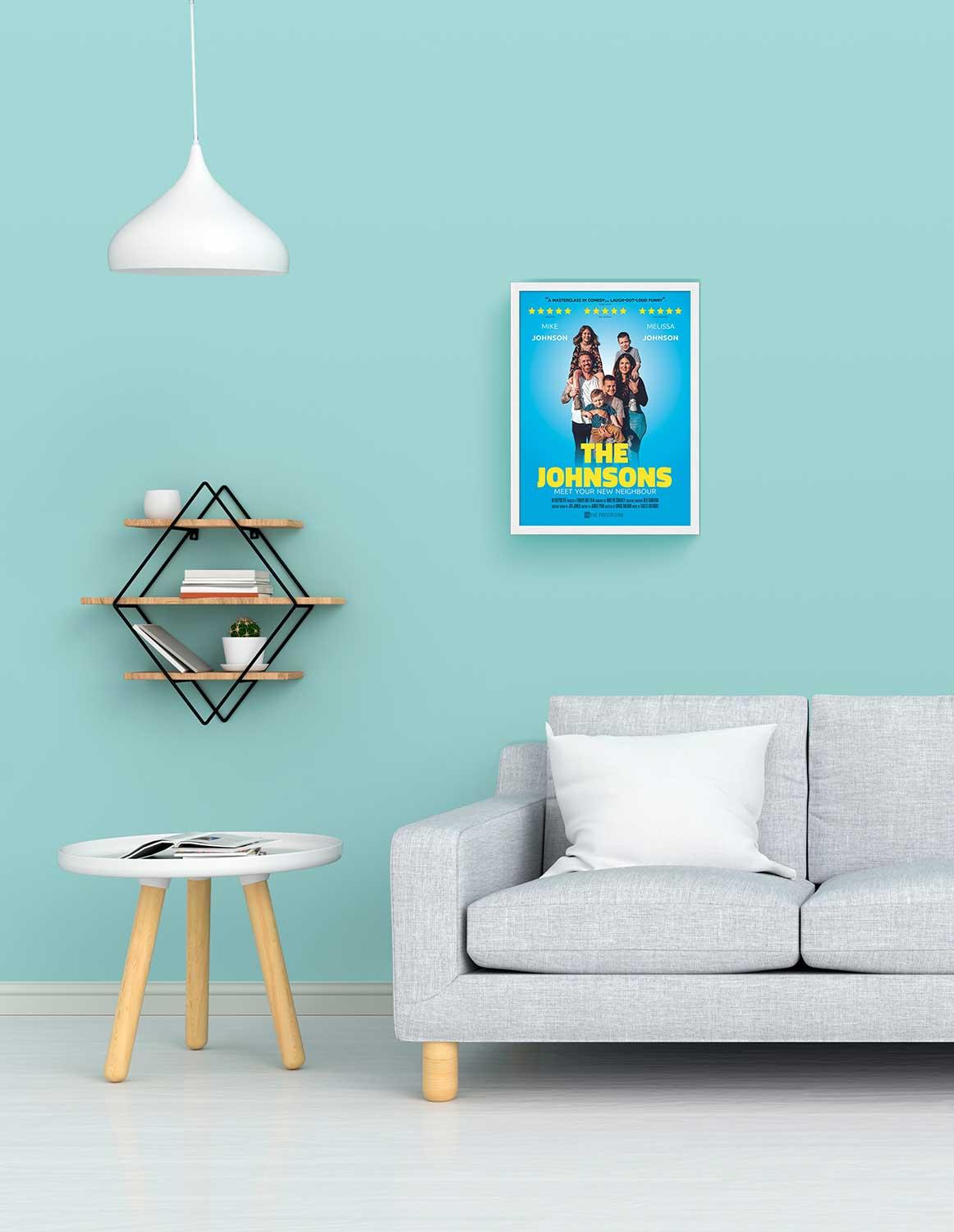 A comedy poster in a small size white frame on the wall above a grey sofa