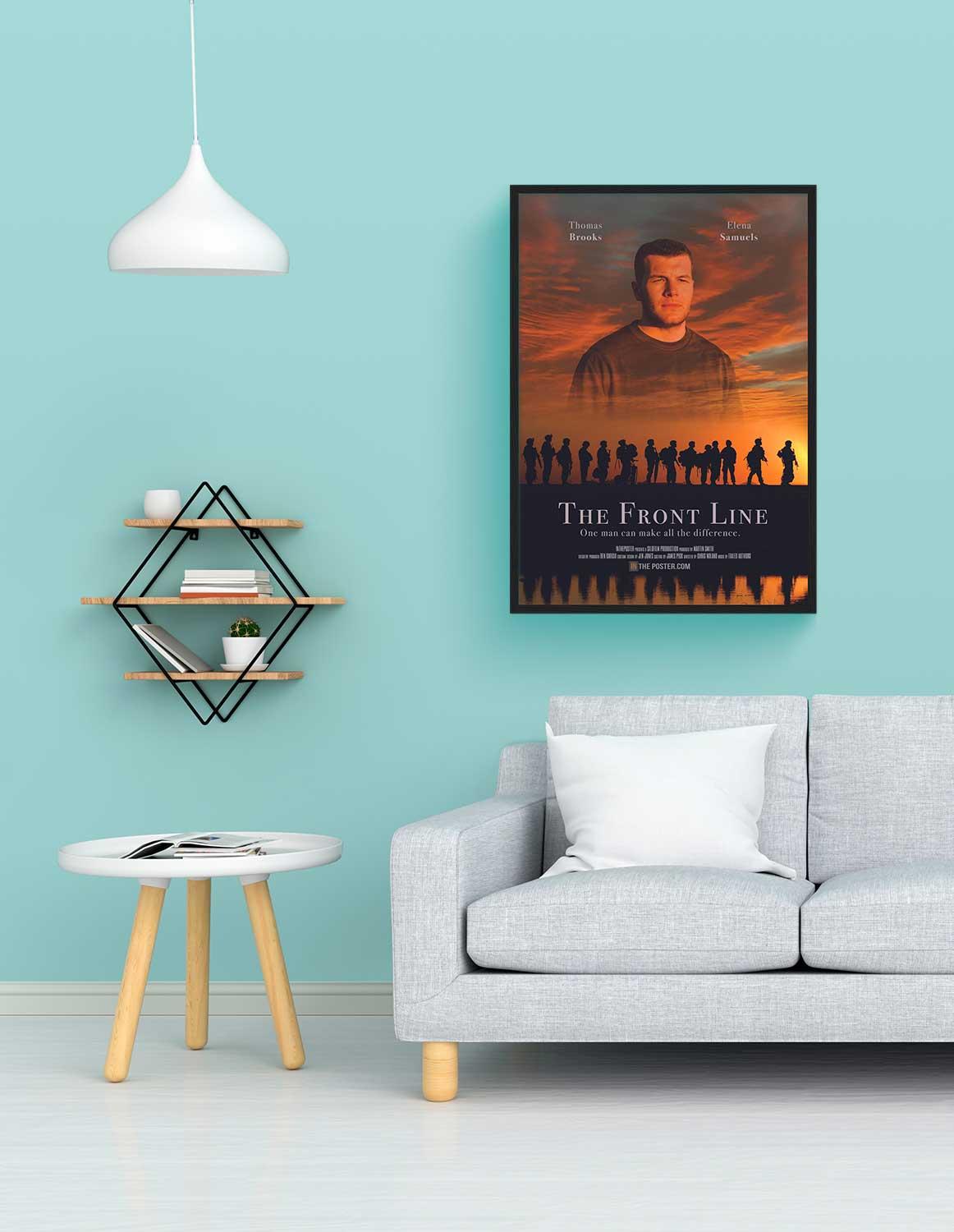 A war movie poster in a regular black frame on the wall above a grey sofa