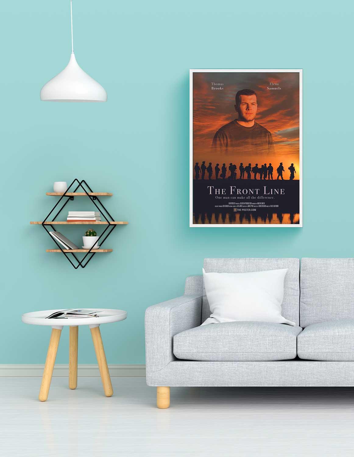 A war movie poster in a regular white frame on the wall above a grey sofa