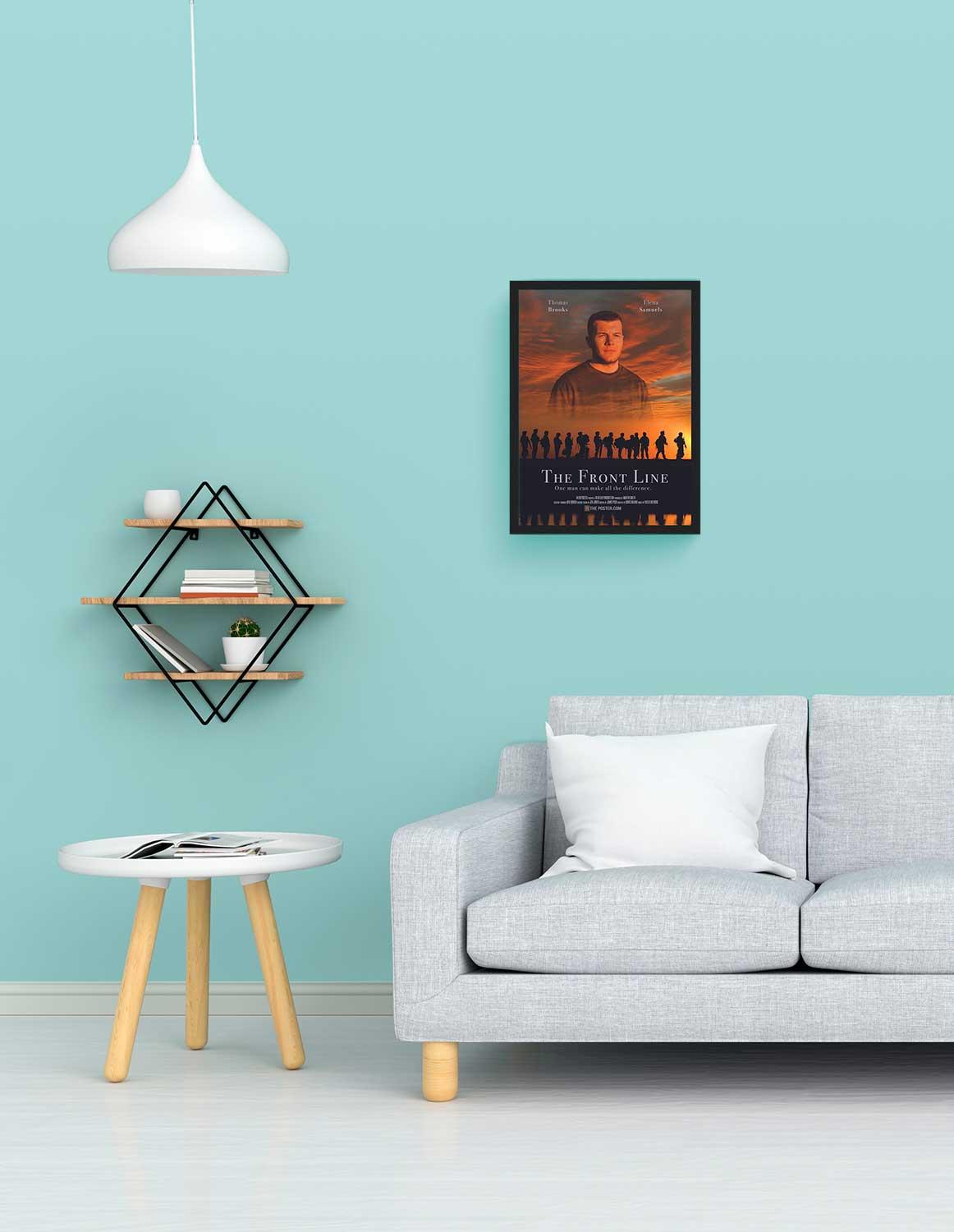 A war movie poster in a small black frame on the wall above a grey sofa